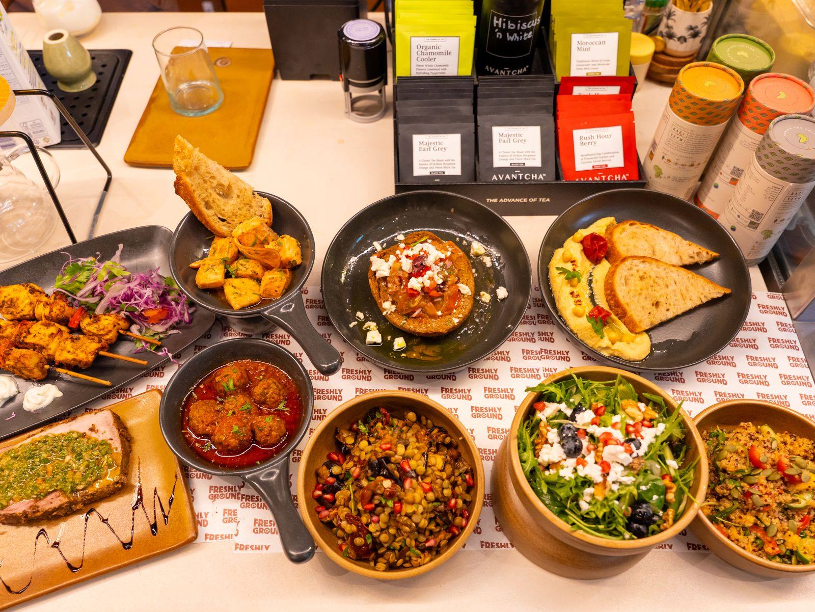 A spread of Freshly Ground dishes including bruschetta, salads and baked eggs laid out on the counter
